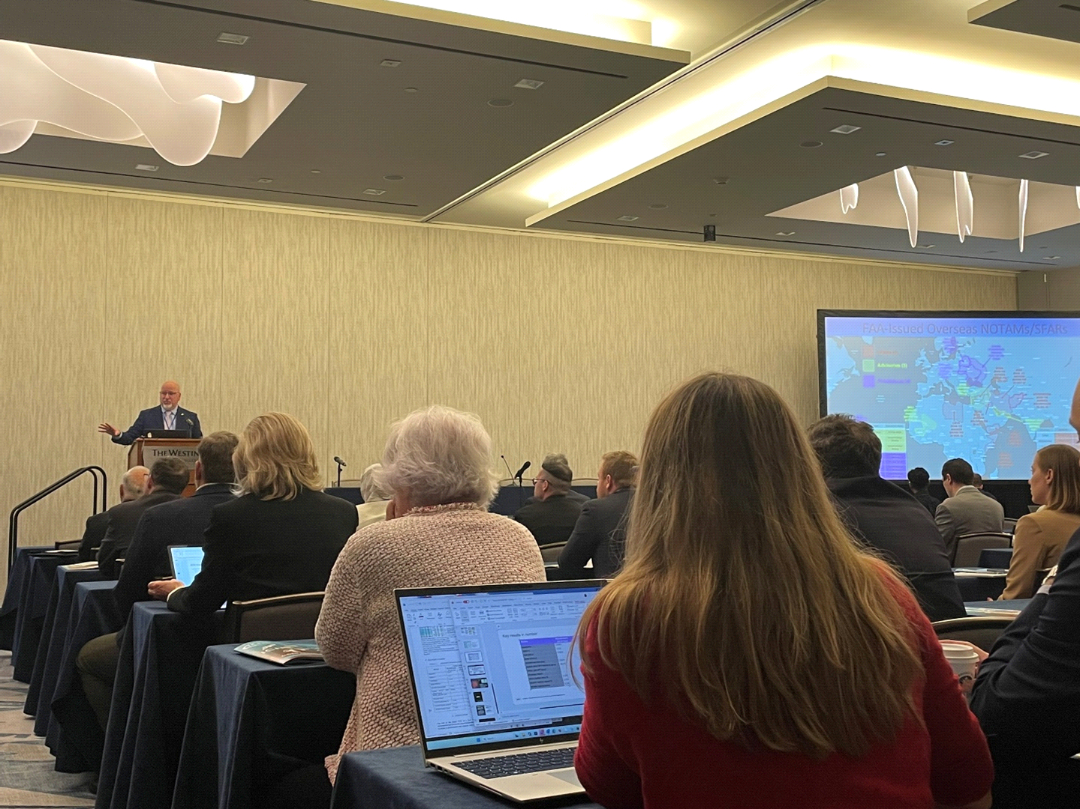Conference attendees listen as an opening keynote speaker presents in the plenary room.