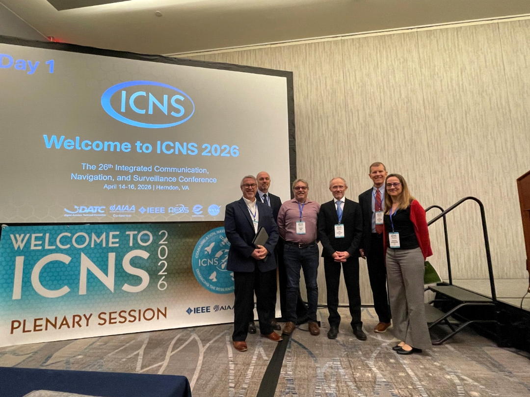 Plenary I participants pose on stage beside the ICNS 2026 welcome screen.