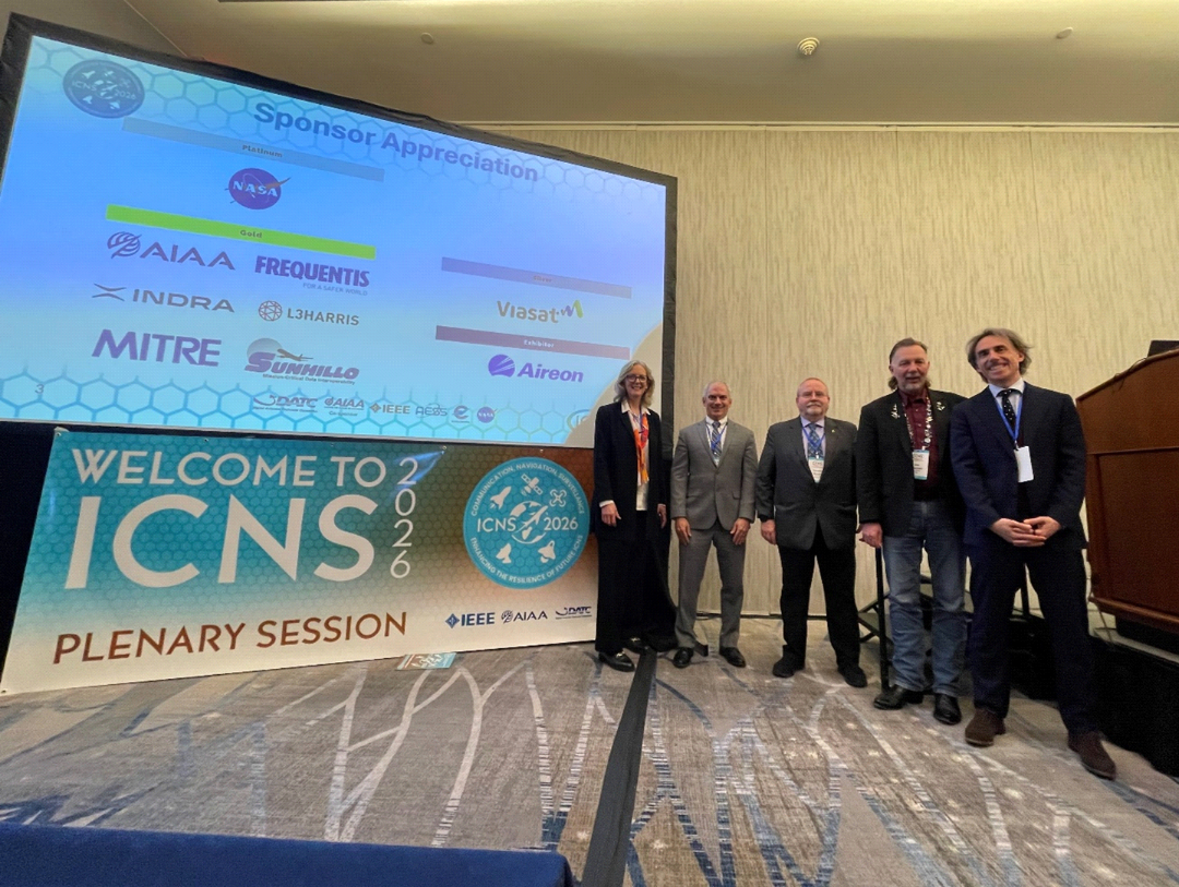 Plenary II participants pose together on stage near the ICNS 2026 session screen.